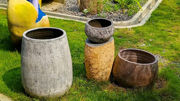 A vibrant outdoor scene featuring four decorative garden pots of various textures and colors, placed on a well-maintained lawn. A partial view of a yellow and blue artistic sculpture is visible too.