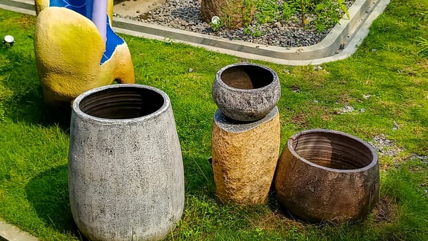 A vibrant outdoor scene featuring four decorative garden pots of various textures and colors, placed on a well-maintained lawn. A partial view of a yellow and blue artistic sculpture is visible too.