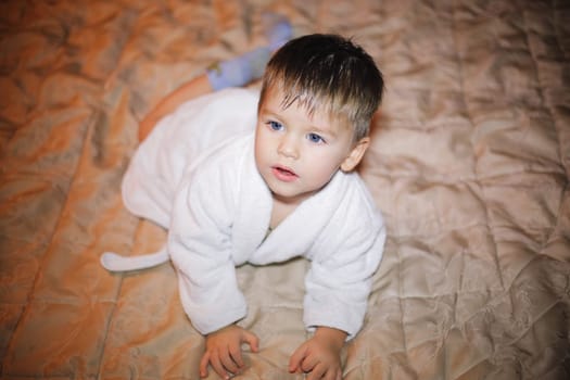 An adorable little baby boy is happily crawling on a soft and cozy blanket while dressed in a white robe