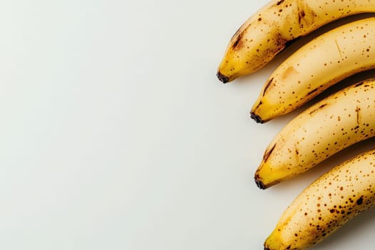 A cluster of ripe bananas lies on a pristine white background, emphasizing their yellow hue and deliciously spotted skin. The smooth texture of the fruit highlights its freshness and ripeness.