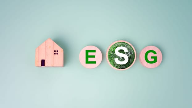 Wooden home and circular wooden board with the abbreviation ESG printed on a light green background, ESG concepts for sustainable environment, Society and governance is environmentally responsible.