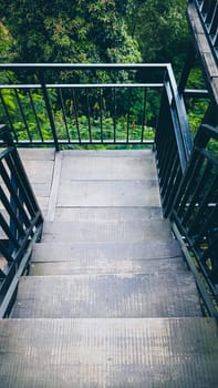 A staircase with a railing and a view of trees. The railing is black and the steps are gray
