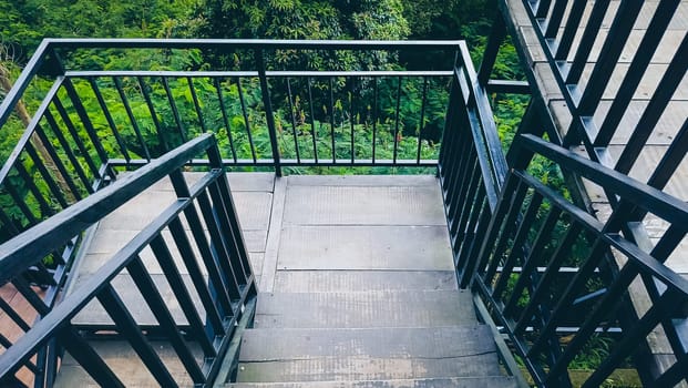A staircase with a railing and a view of trees. The railing is black and the steps are gray
