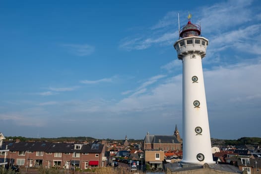 The approx. 28 m high white lighthouse J.C.J. van Speijk in Egmond aan Zee, North Holland, Netherlands with some of the town's houses