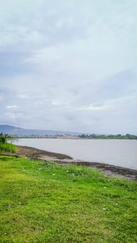 A river with a bridge in the background. The water is calm and the grass is green. The scene is peaceful and serene