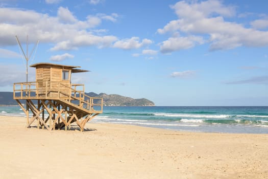 Beach scene with a wooden tower overlooking calm ocean waves and distant mountains, mallorca balearic islands, spain