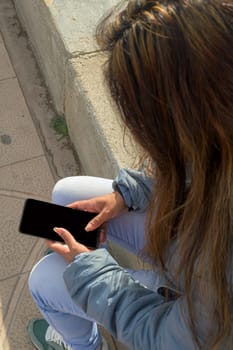 latina woman sitting on a stone bench, looking at a smartphone, dressed casually, mallorca balearic islands, spain