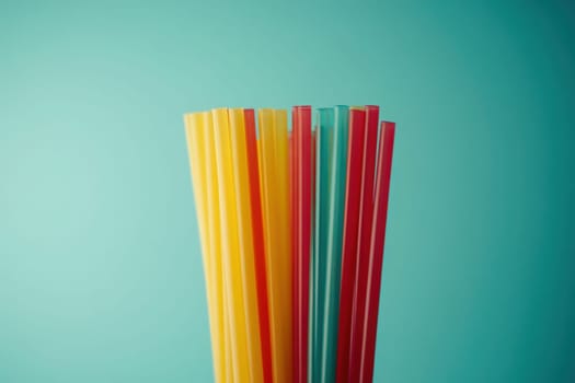 A collection of vibrant straws in yellow, red, and blue stands upright against a soothing aqua backdrop, showcasing a simple and elegant design that emphasizes cleanliness and minimalism.