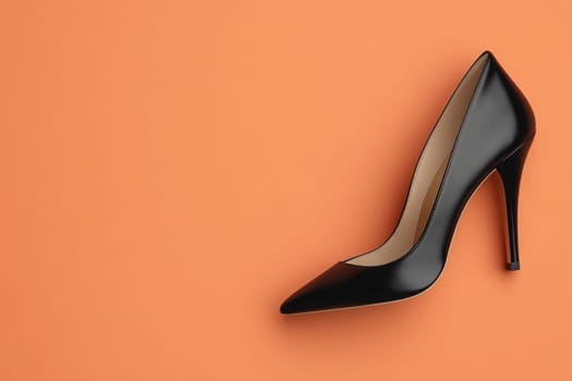 A stylish black high-heeled evening shoe is prominently positioned on a bright orange surface, showcasing its sophisticated design.