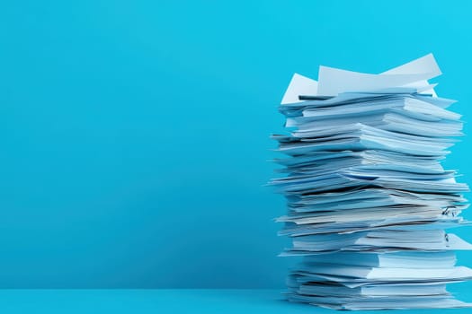 A tall, disorganized stack of unfinished paperwork is resting on a bright blue surface, creating a visual representation of work awaiting attention in a spacious and tidy setting.