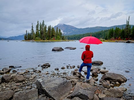 A woman with an umbrella stands by the rocky shore of Lake Wenatchee on a cloudy morning in central Washington.