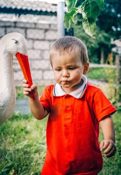 A small child dressed in a bright red outfit happily communicates and plays with a toy stork in a natural environment