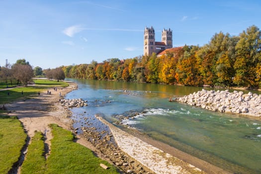 View over Isar River, church and green riparian zone with footpath in autumn in Munich, Bavaria, Germany