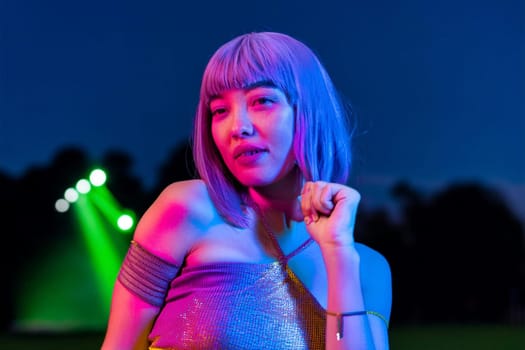 Young Asian woman dancing during outdoor music festival at night.