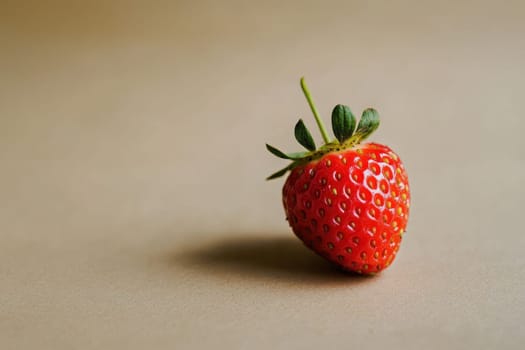 A ripe strawberry rests on a neutral background, showcasing its bright red hue and textured surface. The simplicity of the setting emphasizes the fruits natural beauty and freshness.