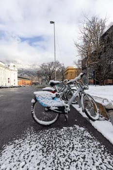 Innsbruck, Austria - February 26, 2023: Snow-covered bicycles parked in Rennplatz square in front of Hofburg, former Habsburg palace. Peaks of the snowy Alps mountains in the clouds in the distance