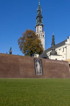 Czestochowa, Poland - October 18, 2024: Tower of Jasna Gora Basilica (Light Mountain) and red brick Jasna Góra embankments with image of Jesus with an inscription: Jesus, I trust in You