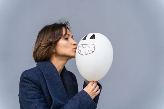 woman kissing balloon with drawn smiley face.