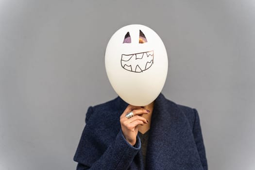 woman holding spooky-faced balloon in front of her own face.