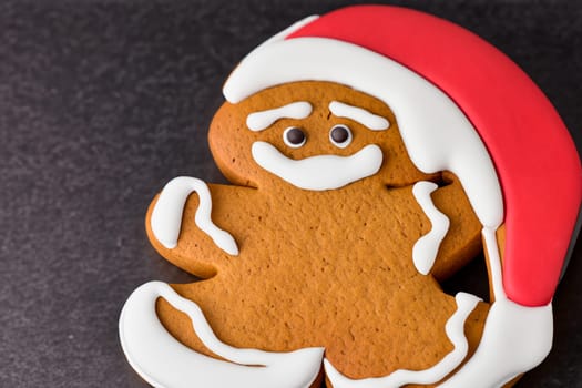 Smiling gingerbread man in Santa hat with black background.