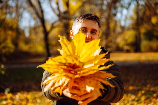 middle-aged man holding maple leaves in front of face in a park.