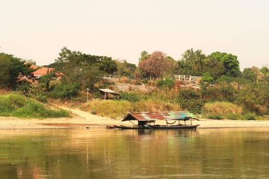 View from the slow boat from Thailand to Laos onto the shore of the Mekong River with a docked river boat, Laos 2023