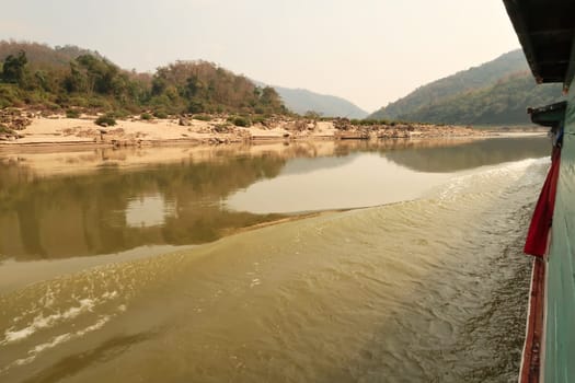 Scenic view from the slow boat from Thailand to Laos onto the Mekong River, the landscape is reflecting on the smooth surface of the water, Laos 2023