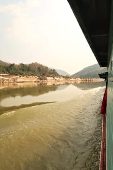View from the slow boat from Thailand to Laos onto the Mekong River, the landscape is reflecting on the smooth surface of the water, Laos 2023
