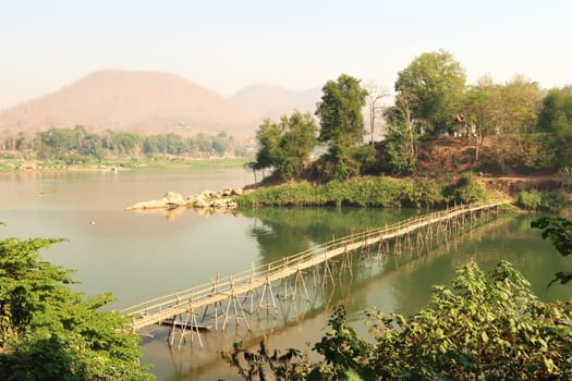 View from the old town on a traditional bamboo bridge over the Nam Khan River, the Mekong River in the background, Luang Prabang, Laos 2023