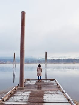 A woman in a coat stands at the end of a dock looking out at the Pend Oreille River in eastern Washington.