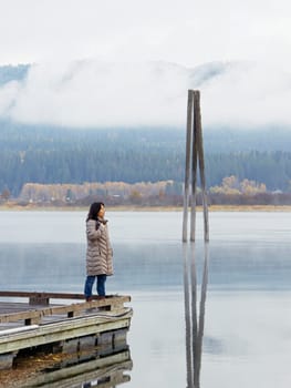A woman stands at the edge of a dock gazing out at the calm Pend Oreille River on a cold morning in eastern Washington.