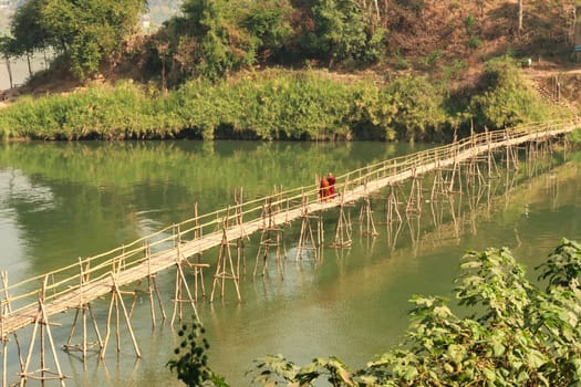 Two buddhist monks cross a traditional bamboo bridge over the Nam Khan River in Luang Prabang, Laos 2023