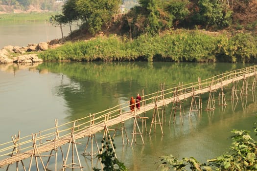 Two buddhist monks on a traditional bamboo bridge over the Nam Khan River in Luang Prabang, Laos 2023