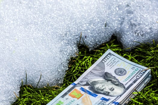 A bundle of cash lying on a snow surface near thawed green grass patch, vividly illustrating themes of financial waste and missed opportunities