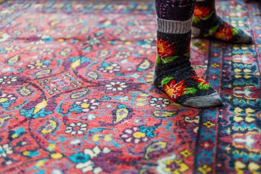 legs in warm woven wool socks standing on red ornate carpet floor at home backlit with a window light