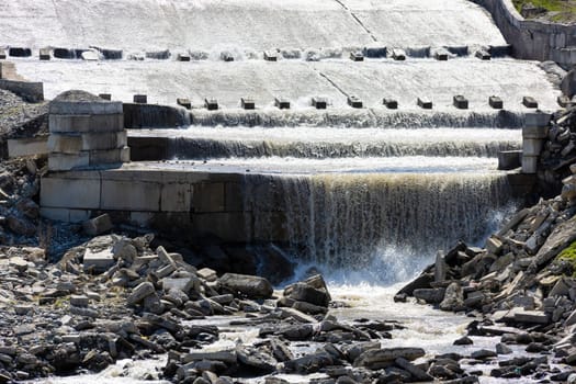 row of chute dentate blocks in cascade concrete water spillway channel slope slowing down the flow of water running down.
