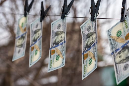 hundred-dollar bills hanging on a clothesline, secured with clothespins, symbolizing money laundering or financial dealings