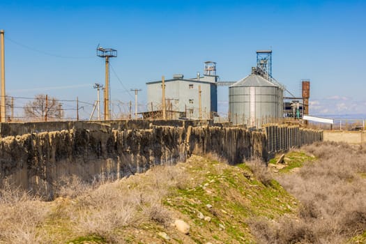 shabby concrete fence with barbwire over and industrial buildings behind at sunny spring day.
