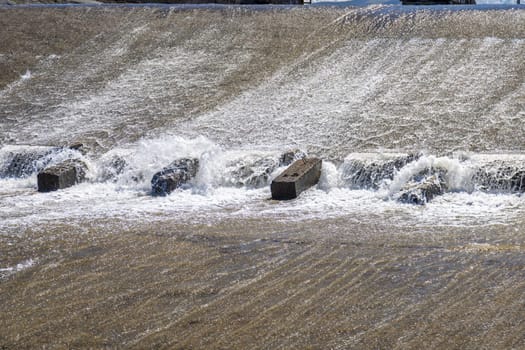 row of chute dentate blocks in concrete water spillway channel slope slowing down the flow of water running down.