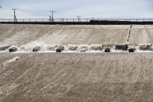 row of chute dentate blocks in concrete water spillway channel slope slowing down the flow of water running down.