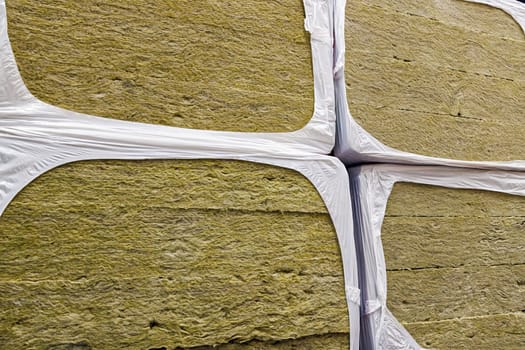Stack of glass wool insulation stacks in white shrink wrap. Stack of fiberglass insulation material. Mineral wool insulator for heat and cold protection.