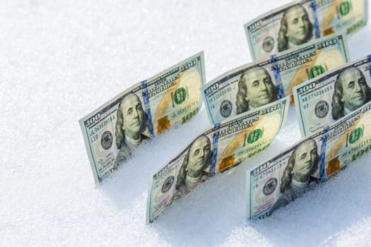 hundred us dollar banknotes standing on their side on the snow surface at sunny winter day
