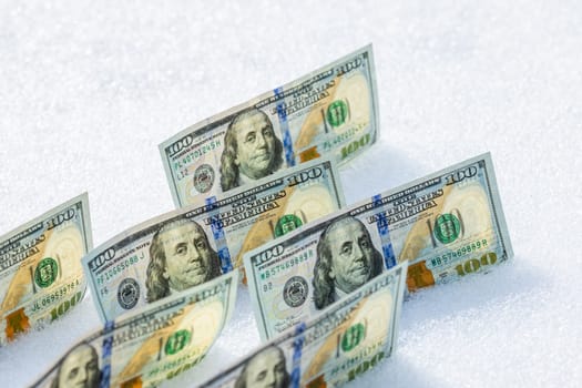 hundred us dollar banknotes standing on their side on the snow surface at sunny winter day