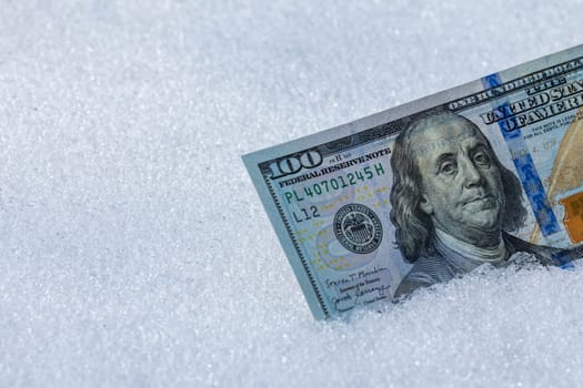 hundred us dollar banknote standing on its side on the snow surface at sunny winter day