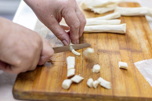 senior woman hand cut horseradish on wooden cutting board with knife