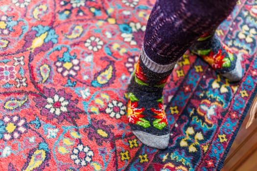 legs in warm woven wool socks standing on red ornate carpet floor at home backlit with a window light