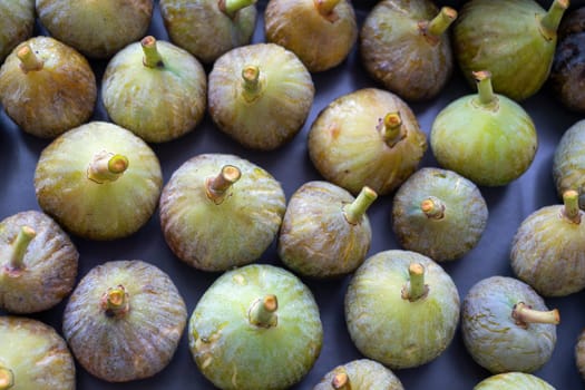 A bunch of green figs are displayed on a table. The figs are small and round, with a stem protruding from the top. Concept of abundance and freshness, as the figs are ripe