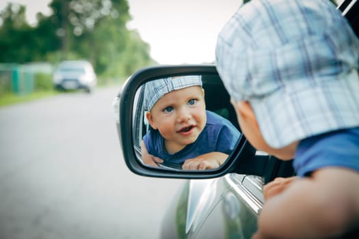 An adorable, playful toddler gazing at their own reflection in a car mirror while enjoying the outdoors