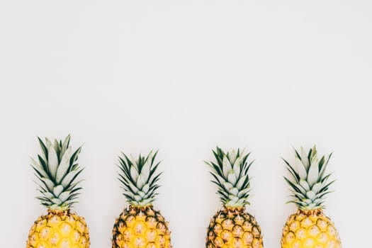 Four ripe tropical pineapples are arranged symmetrically on a clean, solid white surface, highlighting their bright yellow color and lush green tops, perfect for a fresh fruit display.