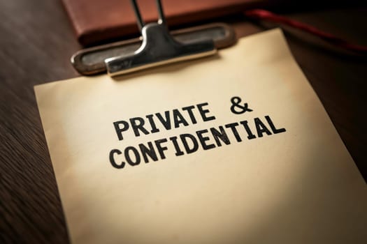 Close-up of a document marked Private & Confidential on a clipboard, symbolizing secrecy, privacy, and sensitive information handling, with a focused, subdued lighting.